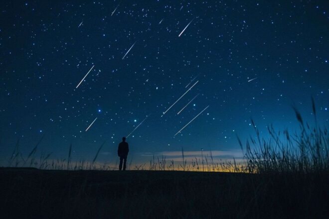 Une vue captivante du ciel nocturne remplie d'étoiles filantes illuminant un paysage paisible, incarnant l'essence de la magie.