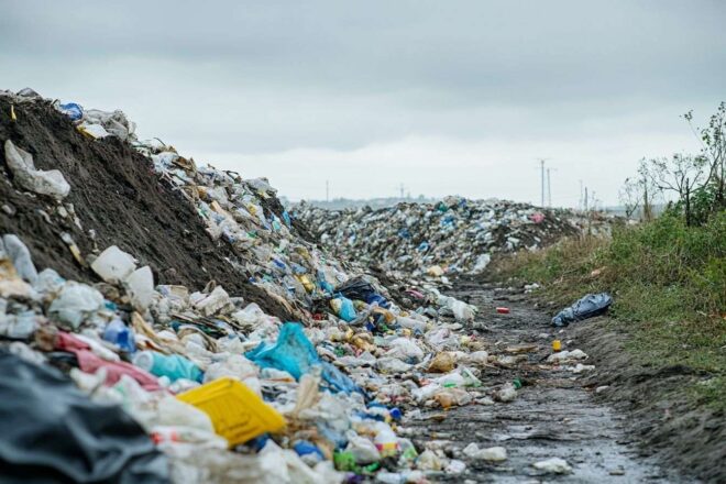 Un site de décharge débordant de débris plastiques sous un ciel gris, illustrant les conséquences de la consommation humaine excessive.
