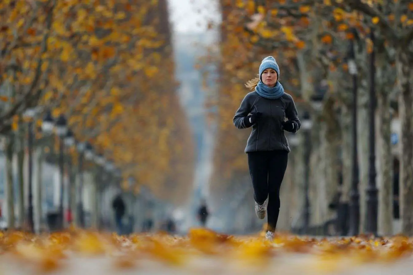 Coureur en tenue d'hiver sur une rue parisienne garnie de feuilles dorées
