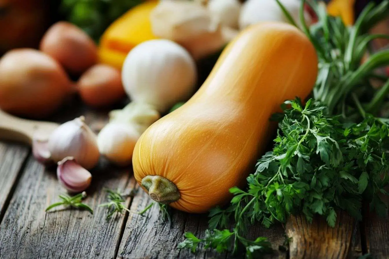 Photo d'une courge butternut colorée avec des herbes et légumes frais sur une table en bois ancien.